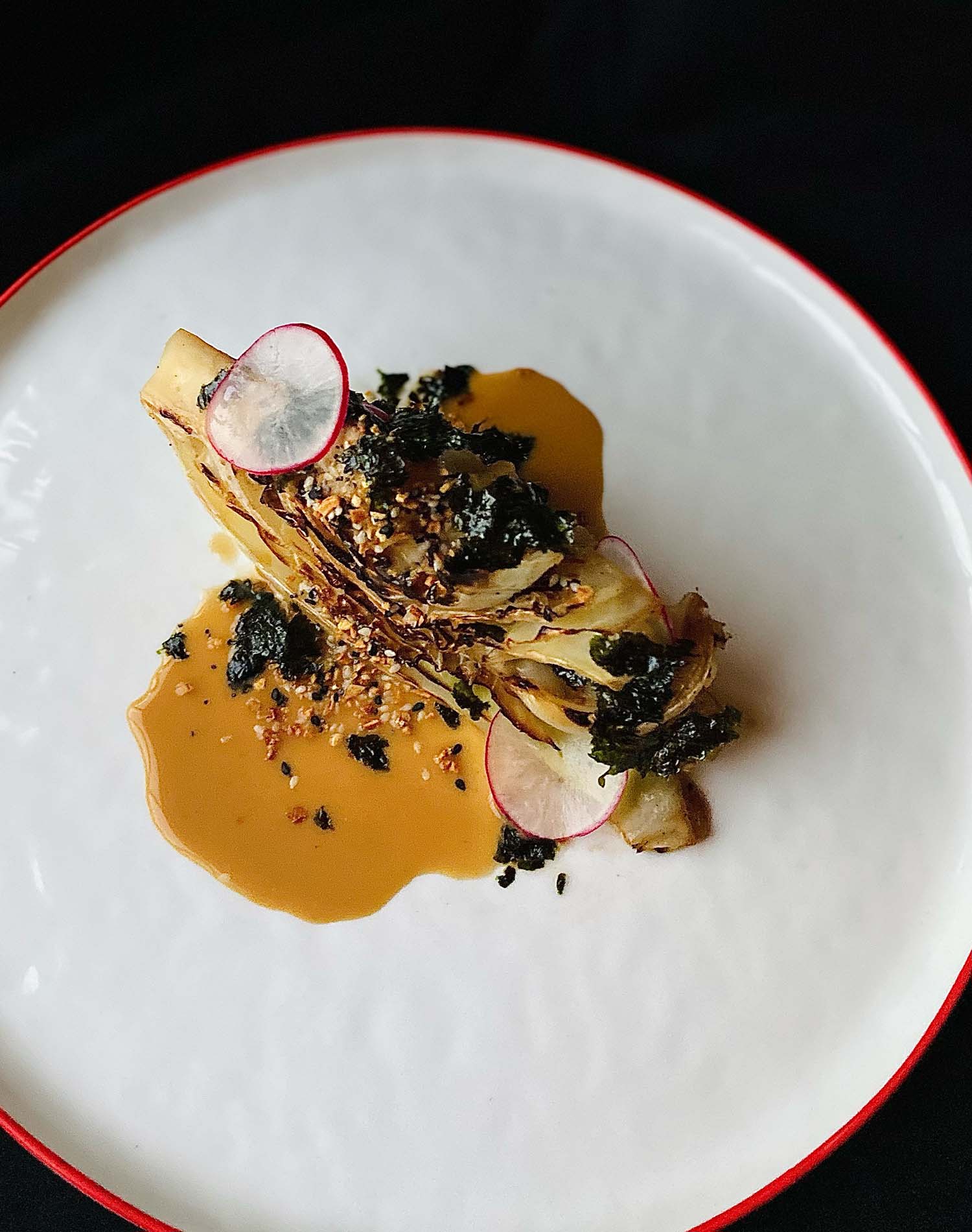 Charred Cabbage with Almond Coconut Yogurt Sauce & Seaweed Furikake Charred cabbage with almond coconut yogurt sauce & seaweed furikake on a white plate with red trim