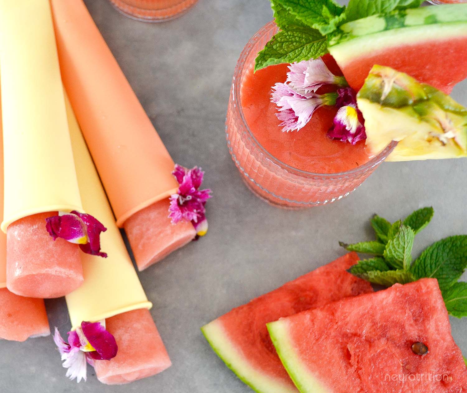 Watermelon Pineapple Coconut Slushie Top view of a watermelon pineapple coconut slushie in a glass with fruit and mint garnishes, beside homemade popsicles and slices of watermelon.