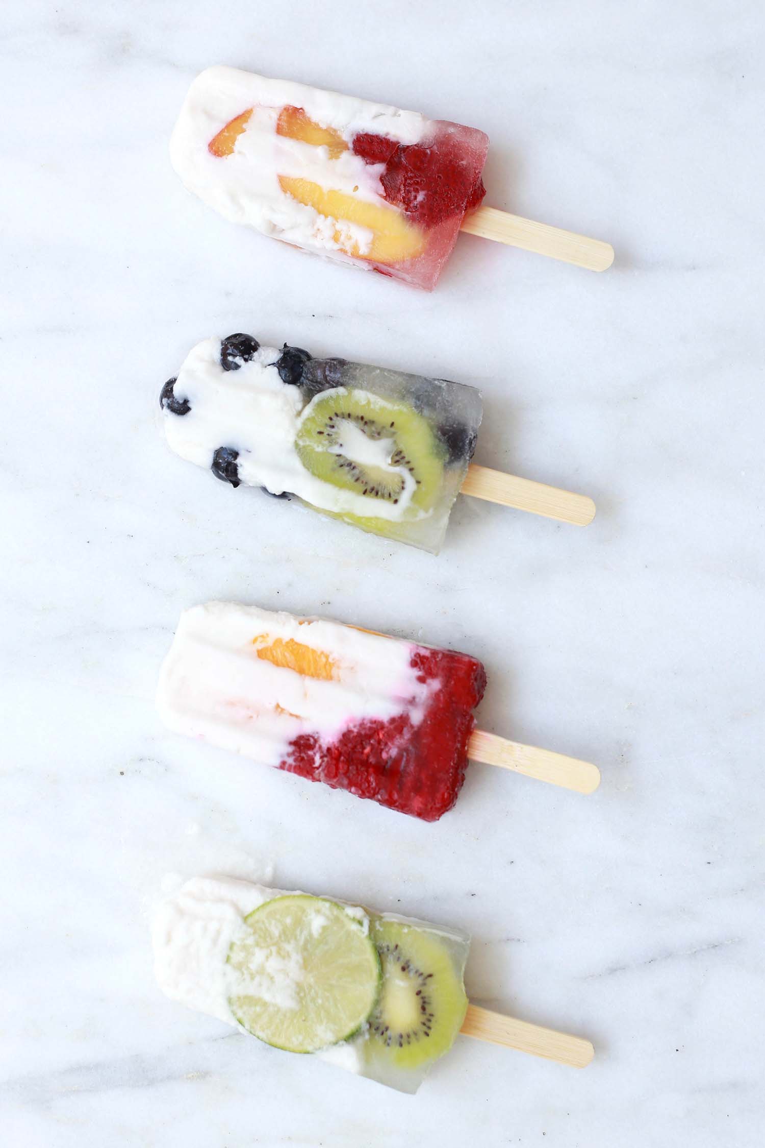Seasonal Fruit Popsicle Four homemade popsicles in a row, with chunks of lime, blueberries, peaches and kiwi