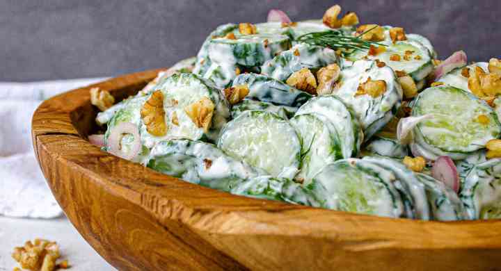 Sliced cucumbers and chopped walnuts in a creamy dressing inside a wooden bowl, topped with dill springs.
